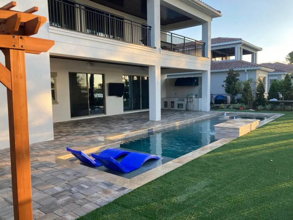 Travertine-coped pool and spa with a paver deck at a luxury two-story lanai