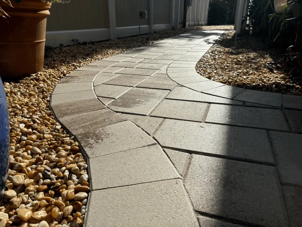 Curved beige paver walkway with a fan pattern and pebble landscaping, freshly sealed